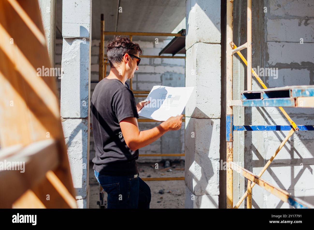 Homme architecte ingénieur vérifiant la maison en construction comparant avec le plan de plan sur papier debout par échelle et échafaudage. Construction de projet w Banque D'Images