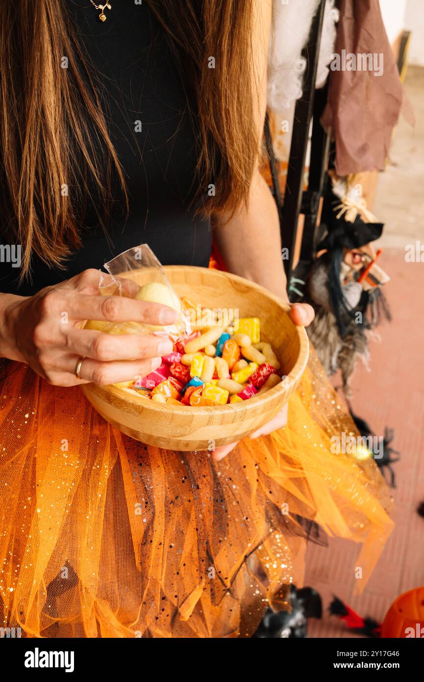 Une femme tient un bol de bonbons et porte une jupe orange. Le bol est rempli d'une variété de bonbons, y compris certains qui sont en forme d'anim Banque D'Images