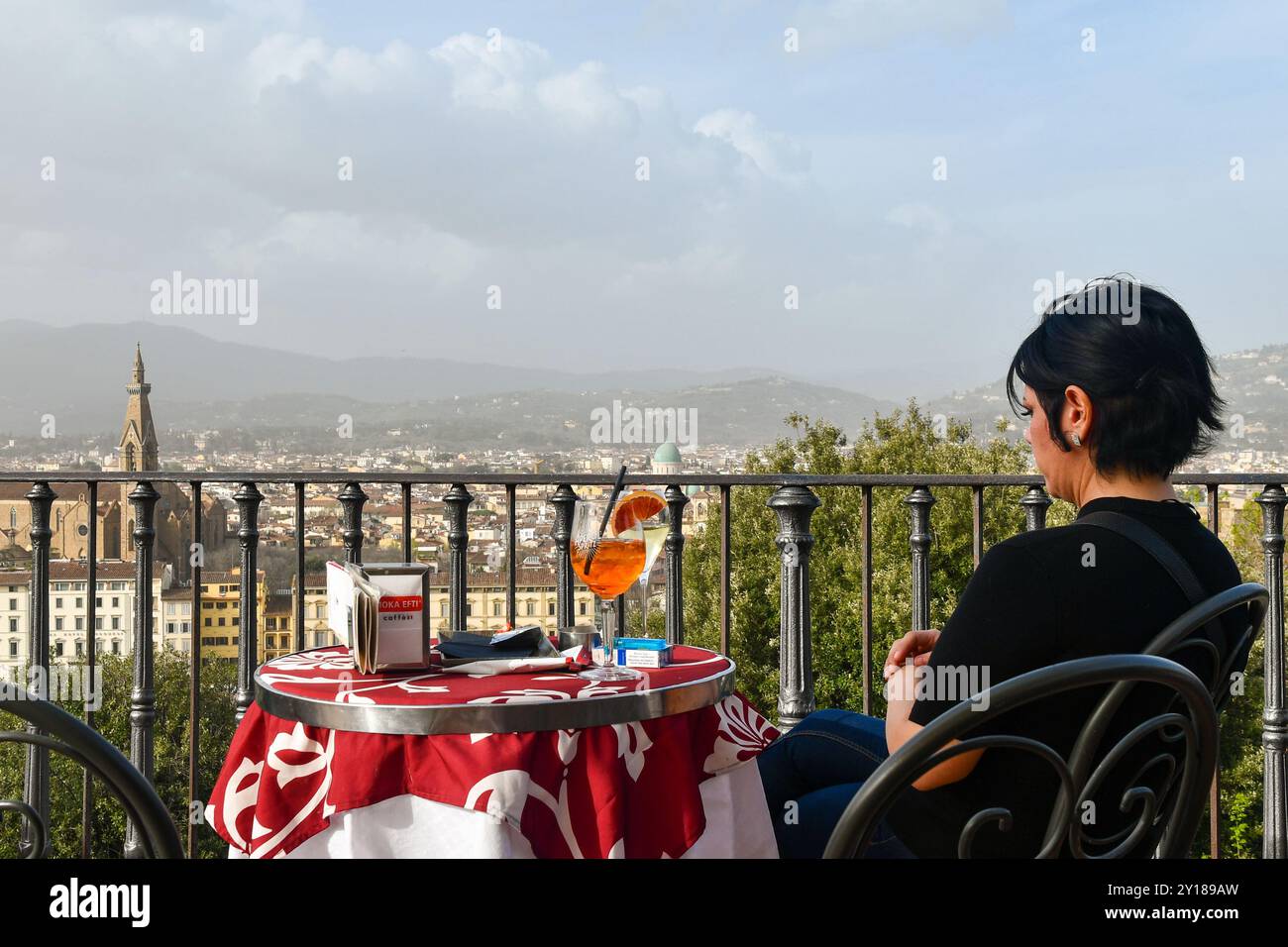 Une femme à une table basse d'un café en terrasse avec un apéritif Spritz et le paysage urbain avec la basilique de Santa Croce en arrière-plan, Florence, IL Banque D'Images