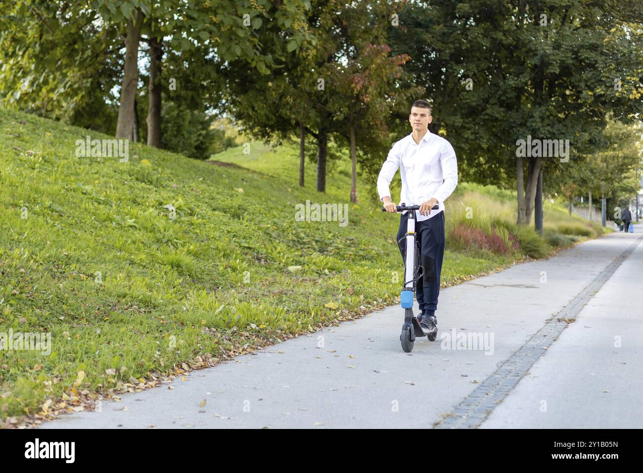 Joyeux et casual man riding scooter électrique dans le parc de la ville Banque D'Images