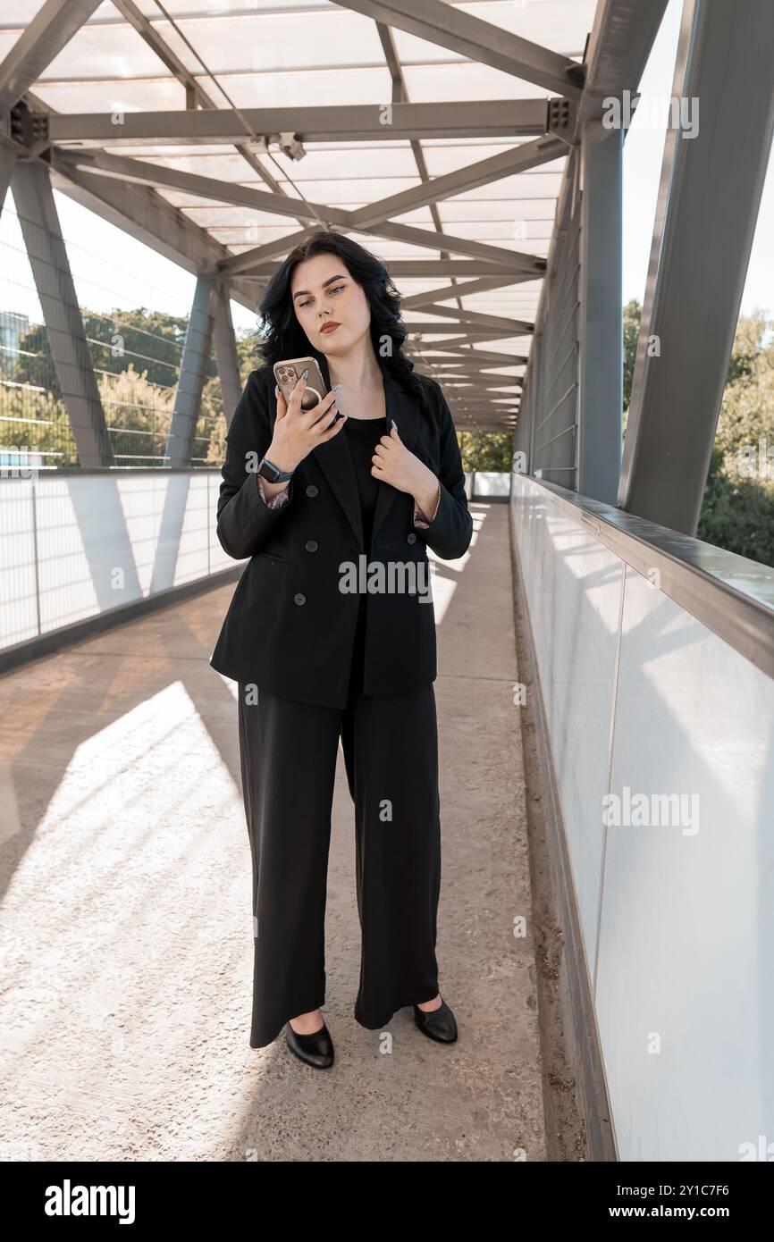 Femme d'affaires confiante avec smartphone sur le pont piétonnier moderne. Banque D'Images