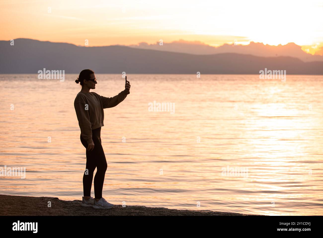 Silhouette d'une femme utilisant un smartphone à Sunset by the Lake Banque D'Images