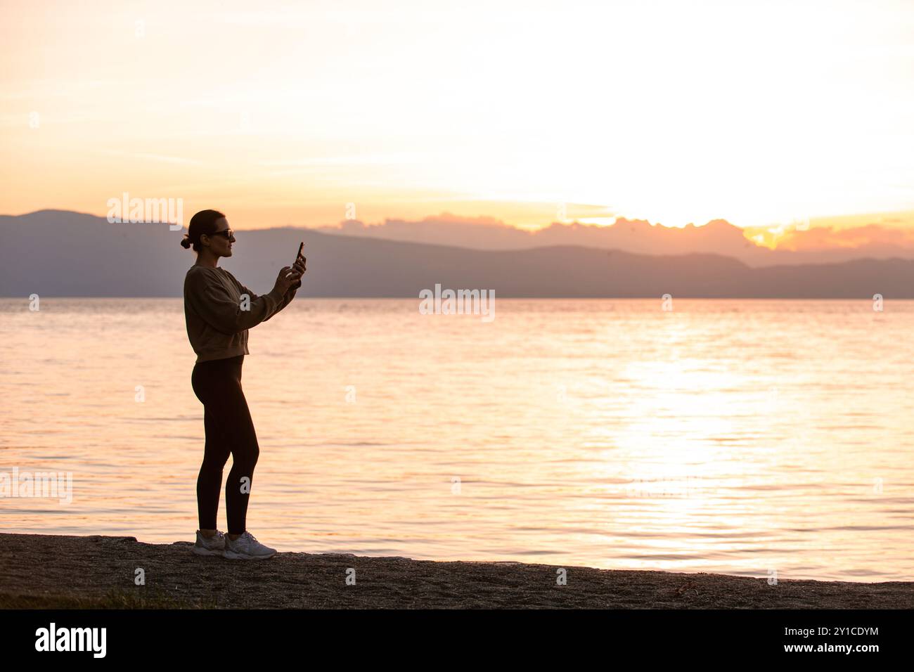 Silhouette d'une femme utilisant un téléphone au coucher du soleil près du lac Ohrid Banque D'Images