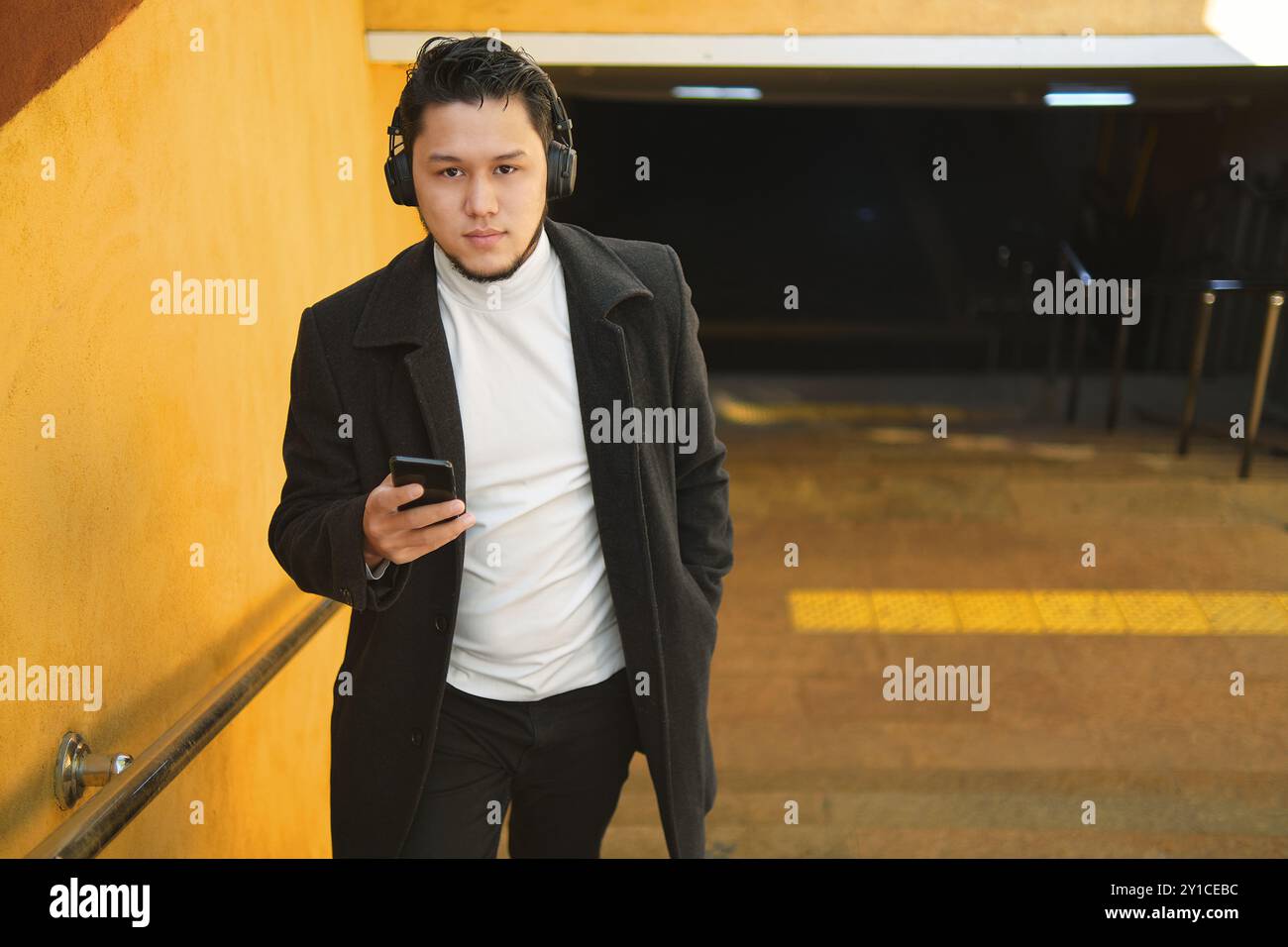 Jeune homme dans les écouteurs vérifiant le téléphone à l'intérieur Banque D'Images