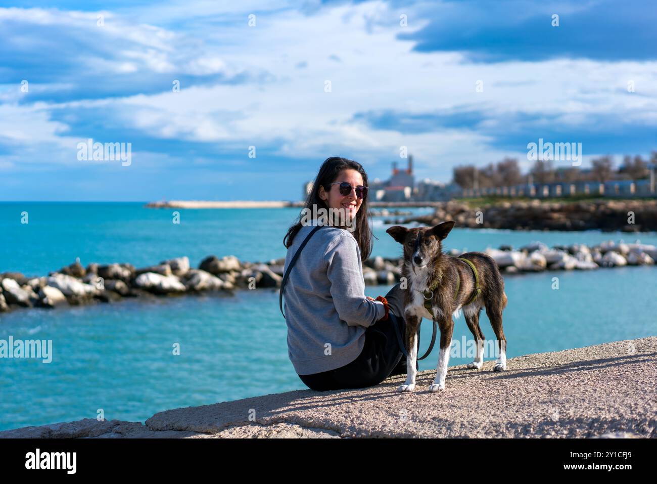 Femme avec chien brun regardant et souriant à la caméra près de la mer Banque D'Images