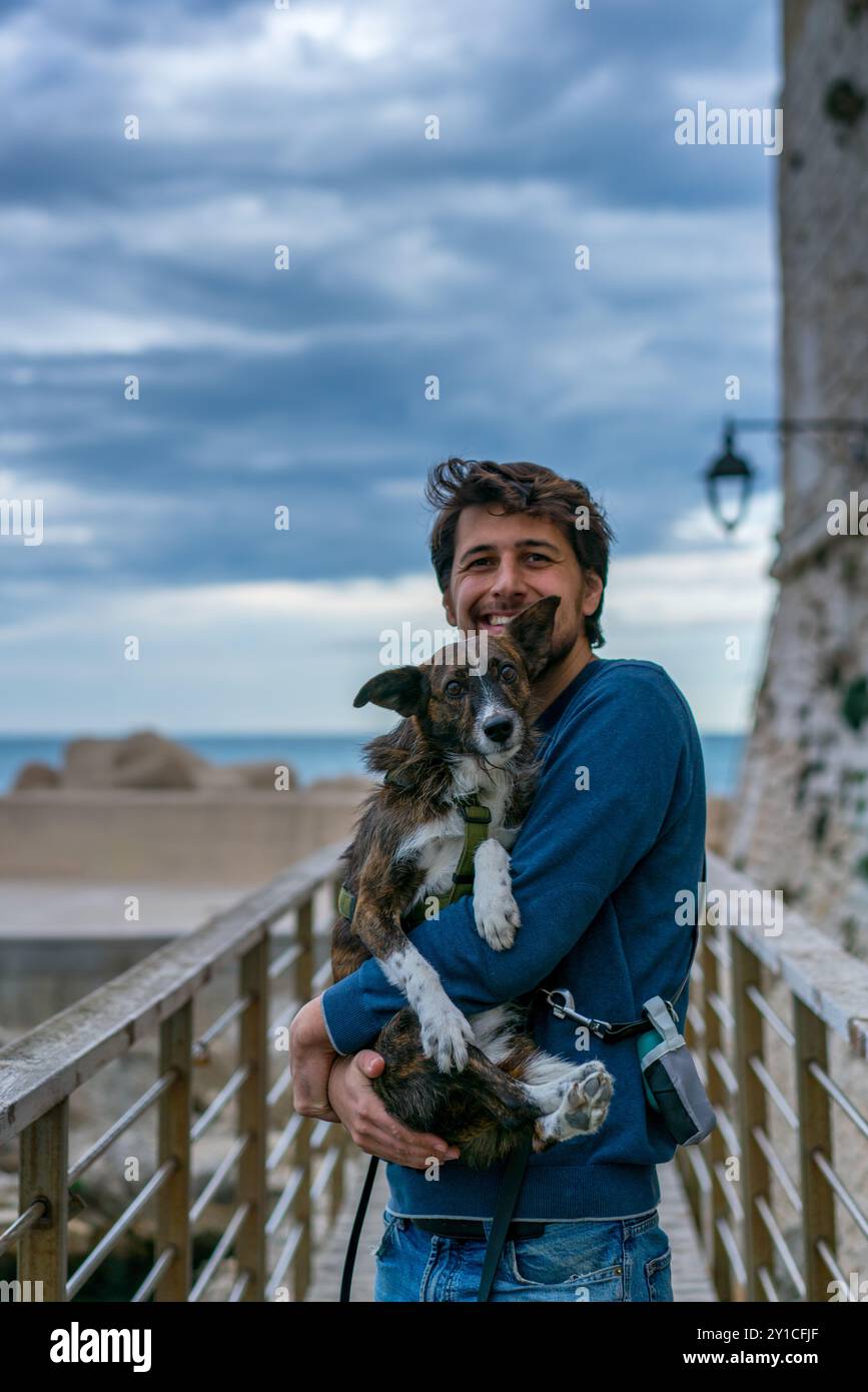 Jeune homme tenant un chien brun dans ses bras souriant à la caméra Banque D'Images