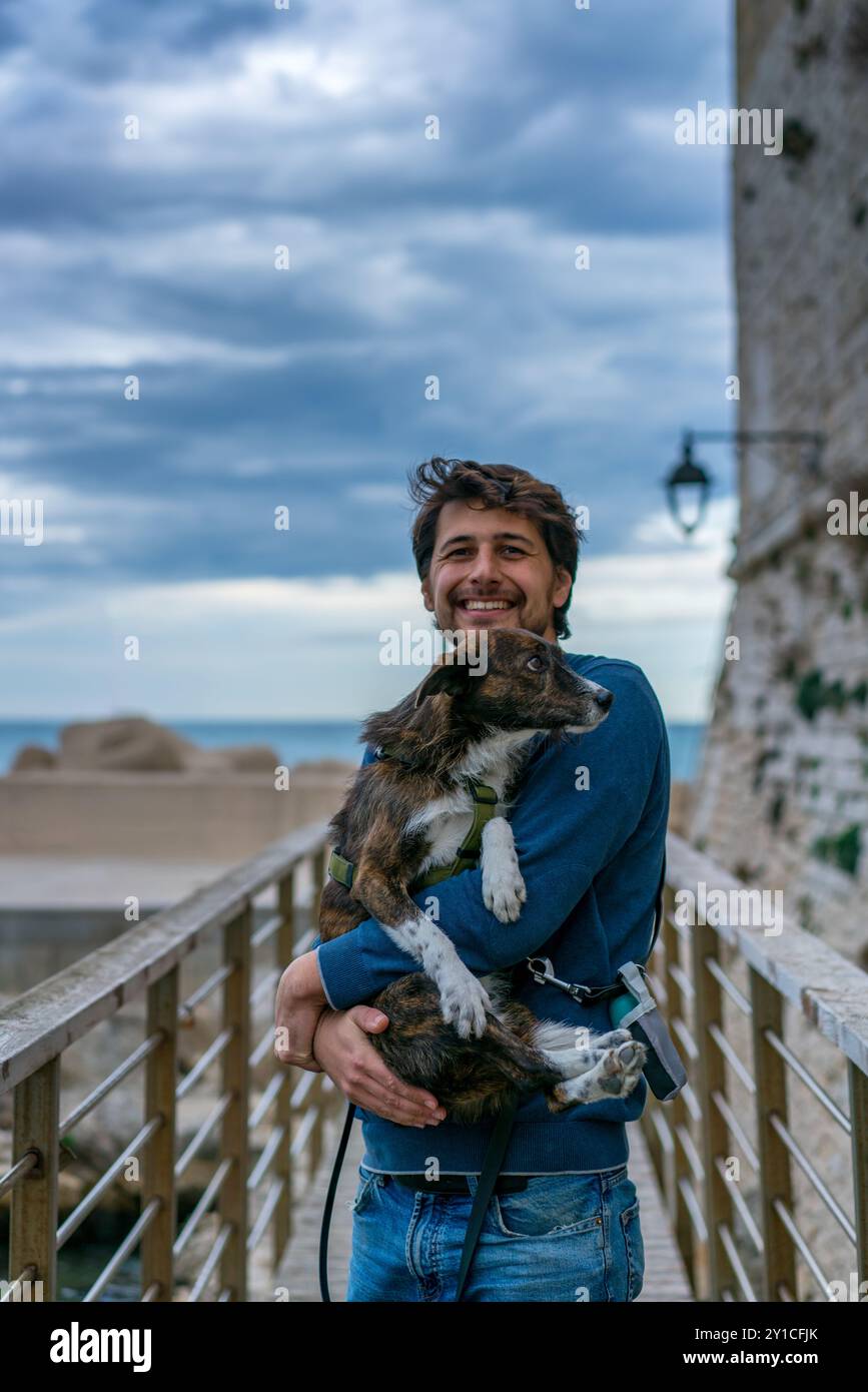 Jeune homme tenant un chien brun dans ses bras souriant à la caméra Banque D'Images