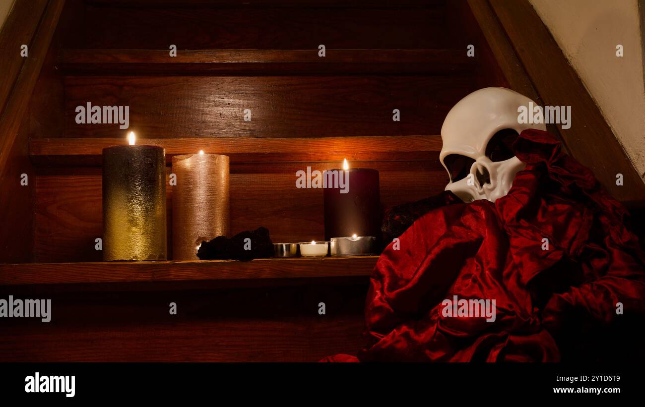 Un crâne sur les escaliers, des bougies, une robe rouge. Spooky Halloween concept. Banque D'Images Un crâne sur les escaliers, des bougies, une robe rouge. Spooky Halloween concept. Banque D'Images