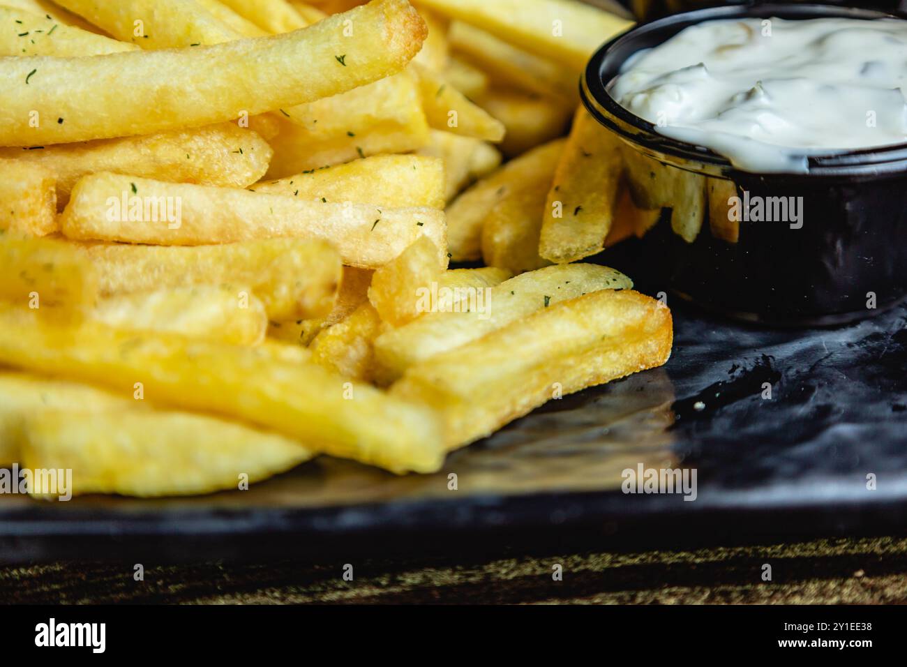 Vue rapprochée de frites croustillantes ou de chips, avec sauce sur une assiette noire Banque D'Images