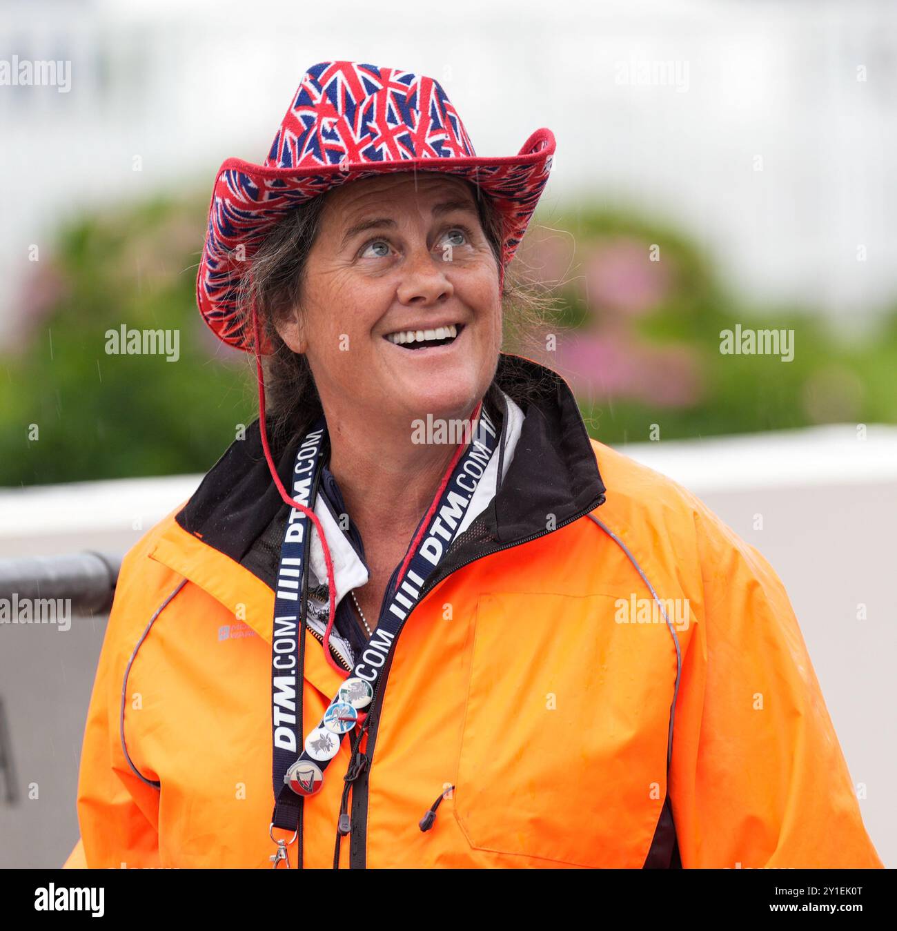 Un marshal de course souriant à Goodwood Revival, un événement immersif de sport automobile vintage. Port d'une veste imperméable orange et d'un chapeau de cow-boy drapeau de l'union (Jack). Banque D'Images