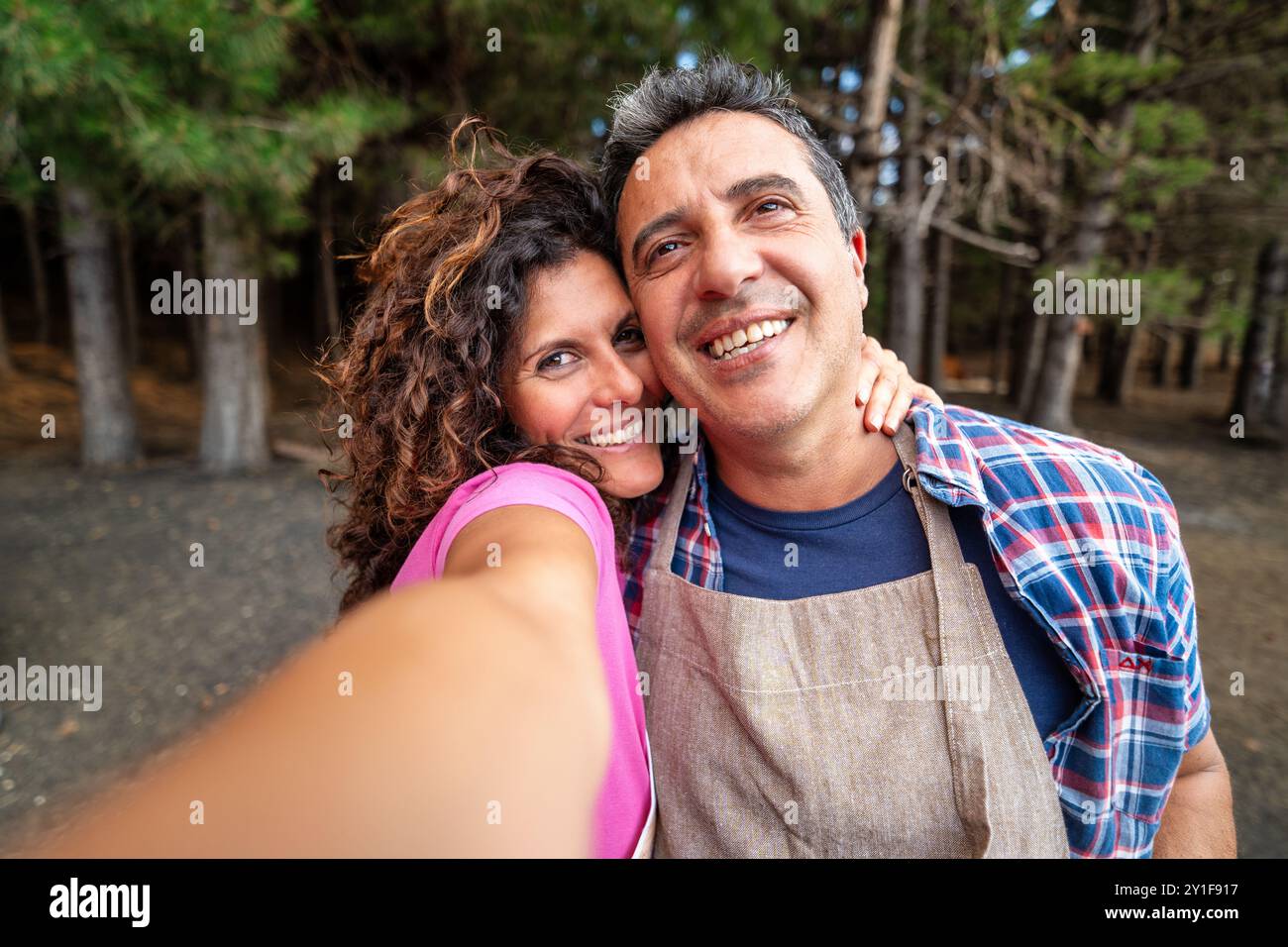 Joyeux couple d'âge moyen prenant un selfie dans une forêt de pins. Sourire homme et femme embrassant, mettant en valeur le bonheur et l'amour dans les relations matures. Ou Banque D'Images