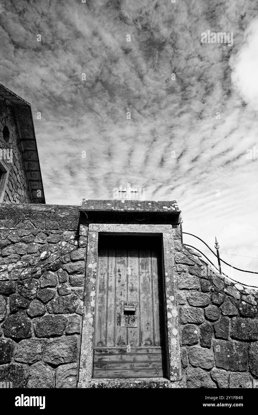 Ancienne porte en pierre couronnée d'une croix altérée sous un ciel saisissant de nuages spectaculaires Banque D'Images