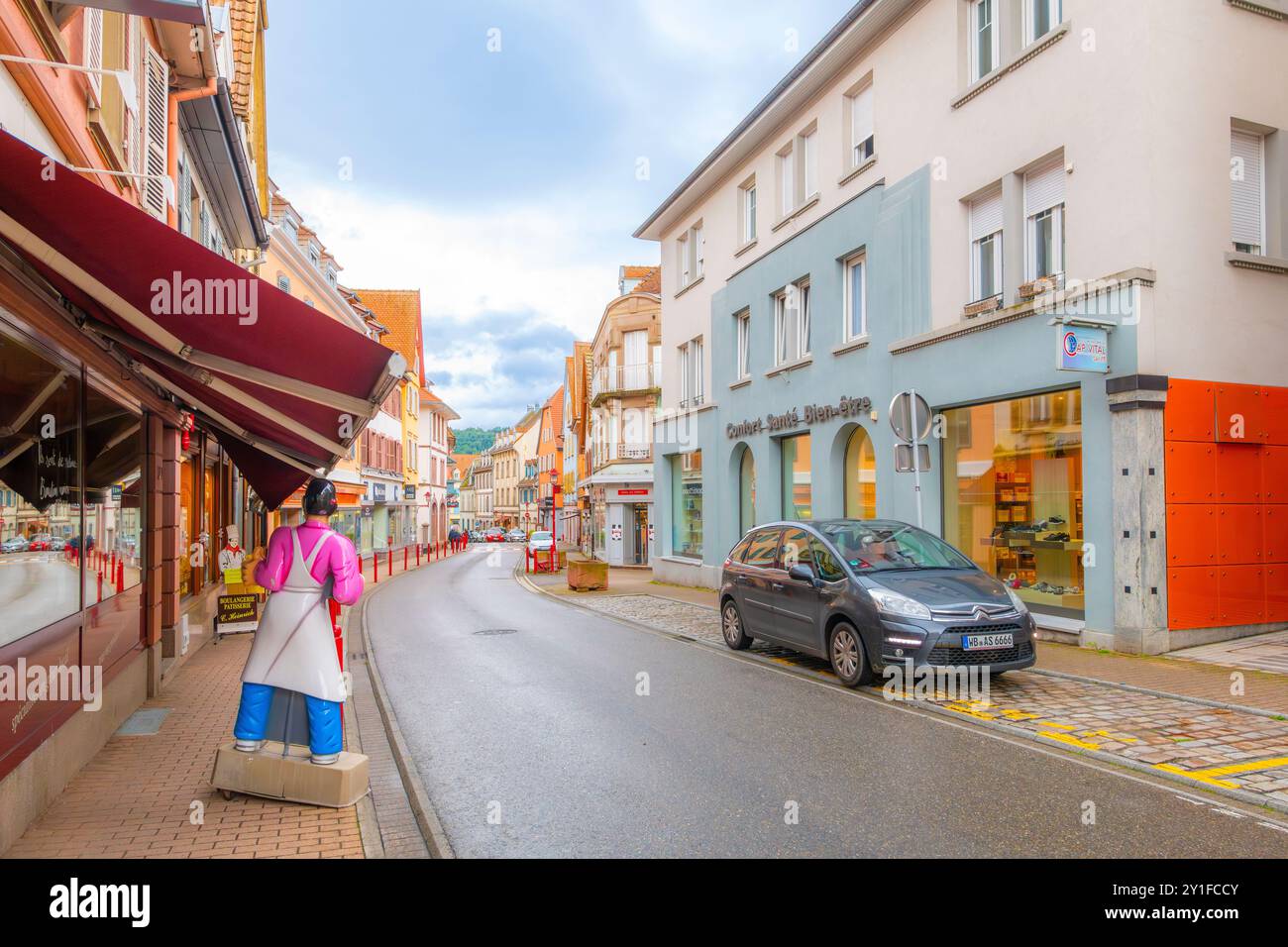 La pittoresque rue colorée de la Grand Rue avec des cafés et des boutiques sur le trottoir dans la vieille ville historique de Munster, en France, dans la région viticole d'Alsace. Banque D'Images