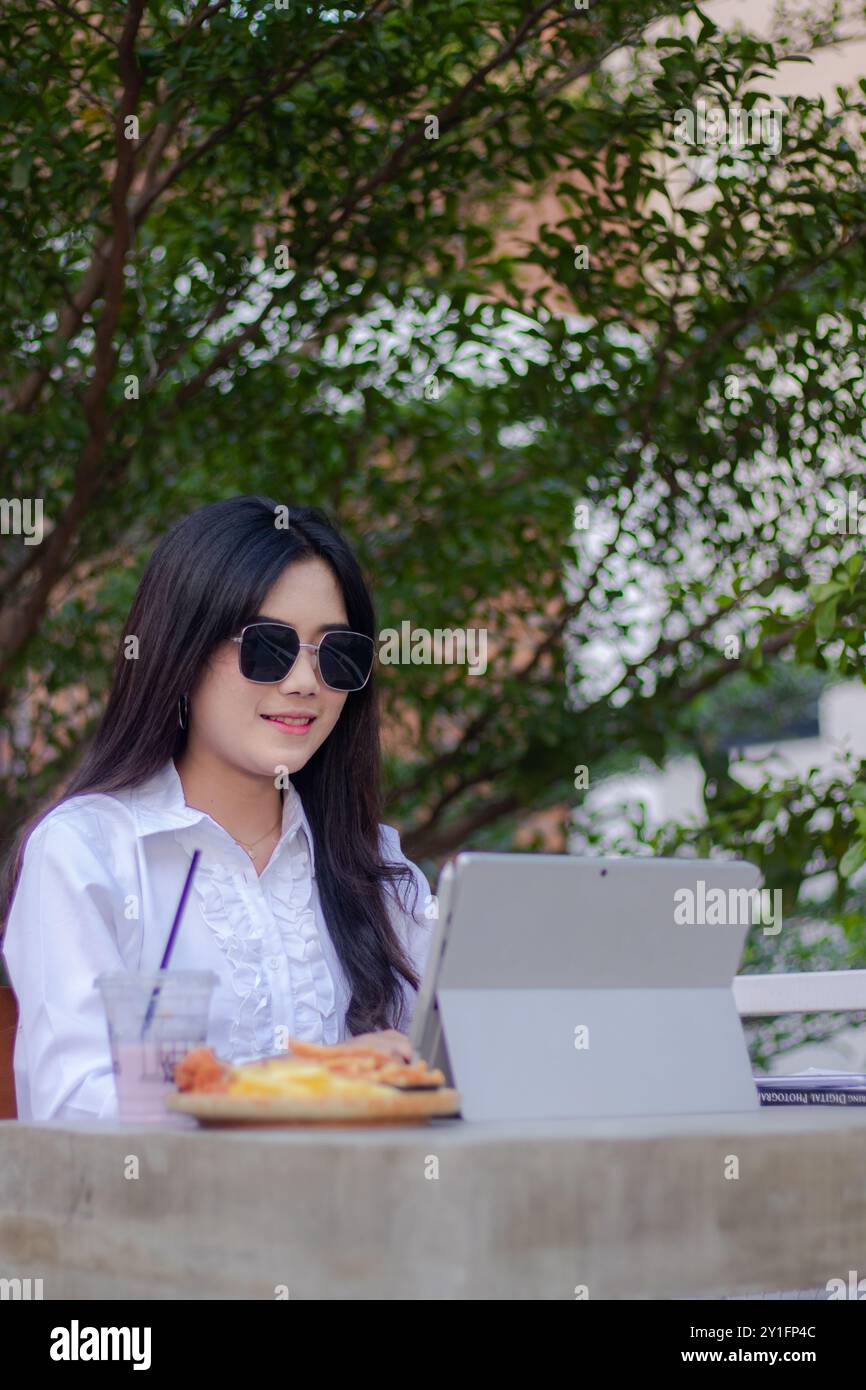 bureau belle femme asiatique dans un café en plein air. fille souriante faisant le travail sur ordinateur portable dans des lunettes de soleil candid pour le contenu ou la publicité Banque D'Images
