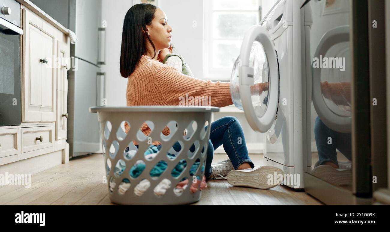 Mère, bébé et panier dans la cuisine pour machine à laver, ménage ou maternité dans la maison avec enfant. Femme, nouveau-né et chargement du linge pour Banque D'Images