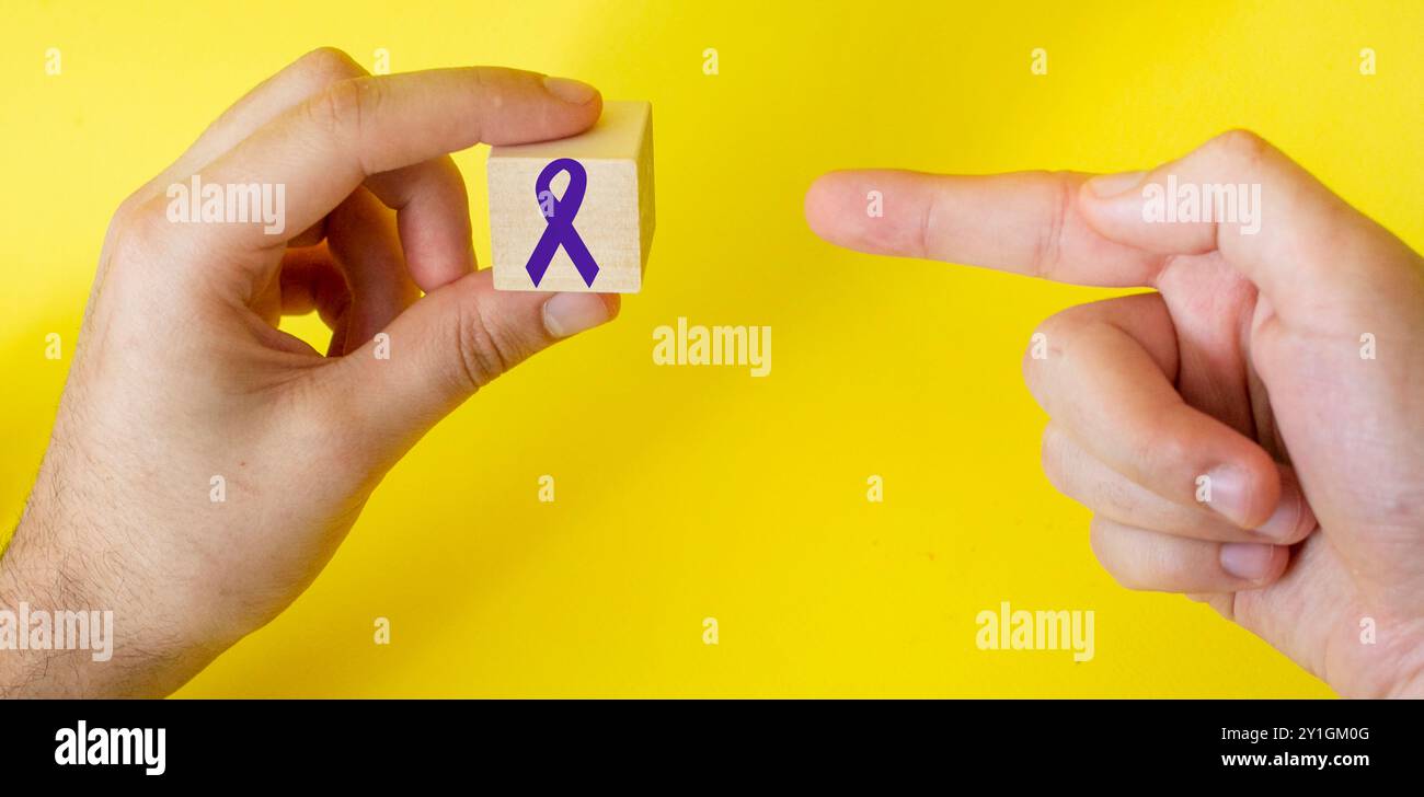 Ruban violet sur un cube montre un doigt sur un fond jaune. À l'appui de la campagne de la Journée mondiale contre le cancer et de la Journée Alzheimer. Banque D'Images