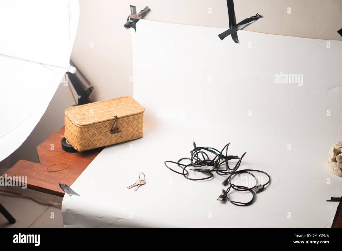 Une installation photographique minimaliste avec un fond blanc, un panier tissé, des câbles dispersés et une paire de touches sur une surface en bois. La scène est bien Banque D'Images