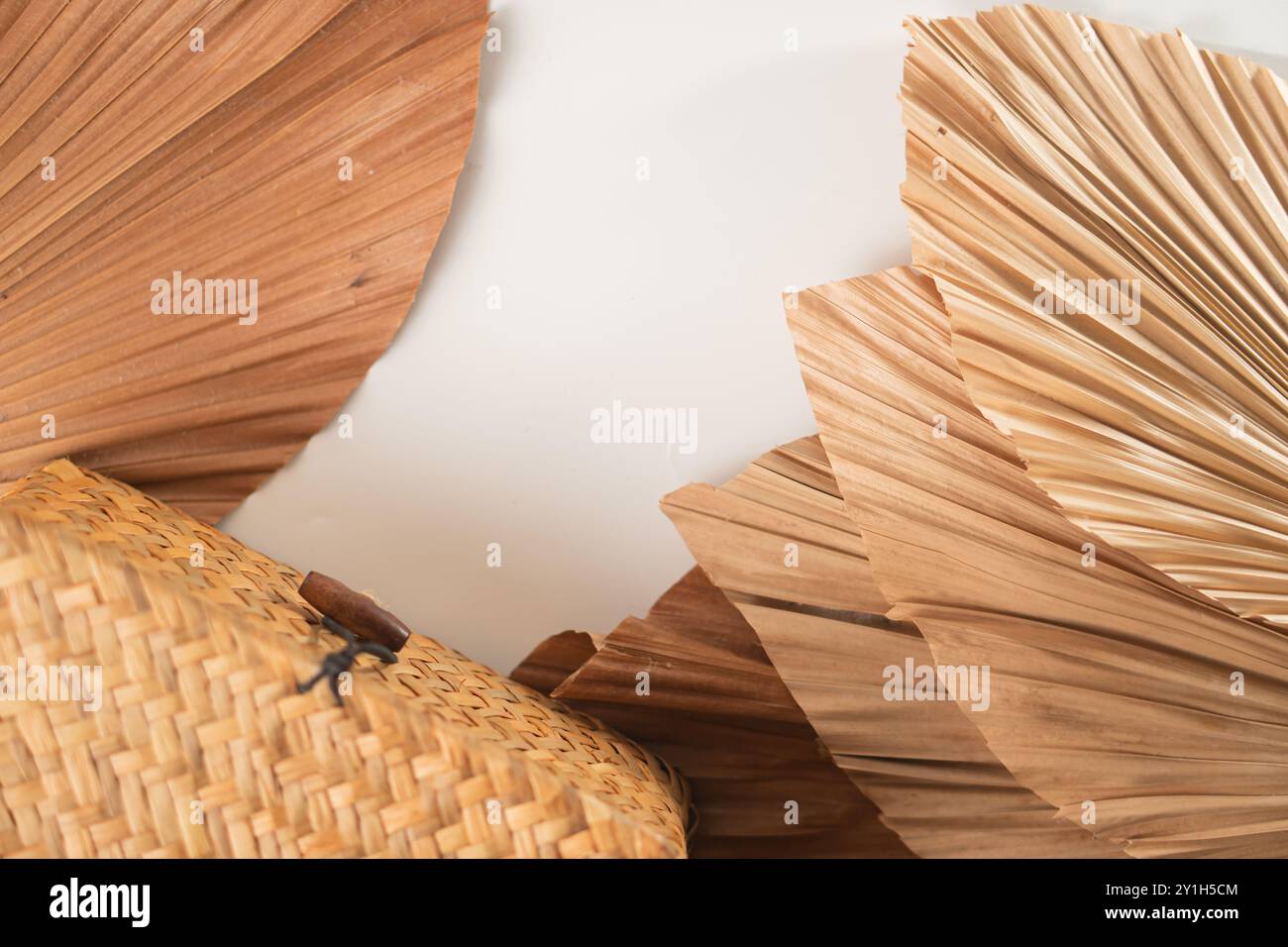 Une couche plate de feuilles de palmier séchées disposées artistiquement autour d'un panier tissé. Les textures naturelles et les tons terreux créent une esthétique chaleureuse et organique. Banque D'Images