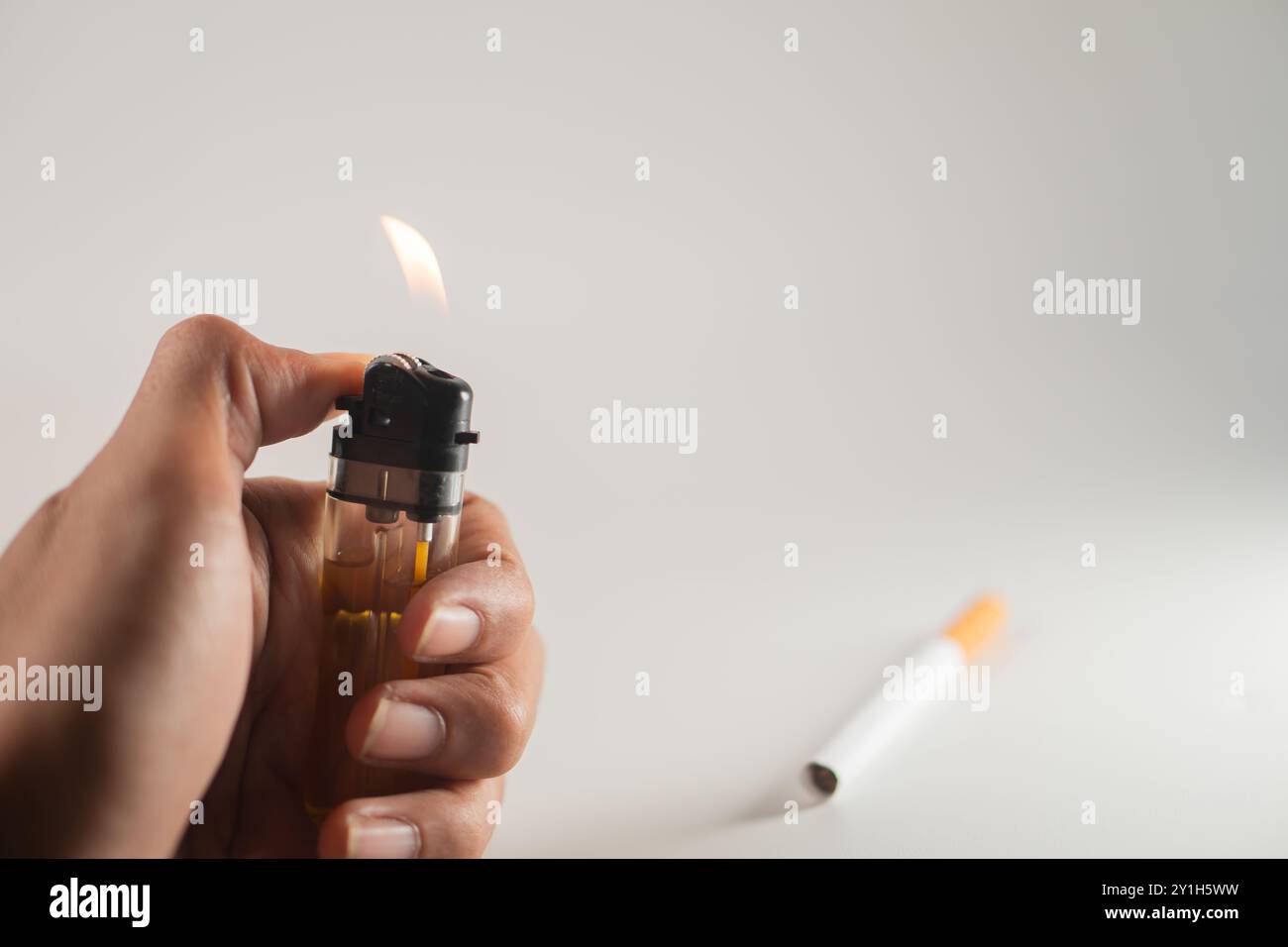 Une main tenant un briquet avec une flamme allumée, posée sur un fond Uni. Un stylo blanc avec une pointe orange est placé à proximité. Banque D'Images