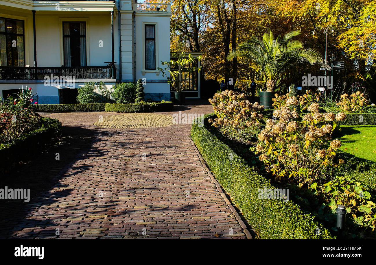 Un pittoresque chemin de jardin bordé de haies soigneusement taillées et de fleurs en fleurs, menant à une charmante maison entourée de feuillage d'automne. Banque D'Images