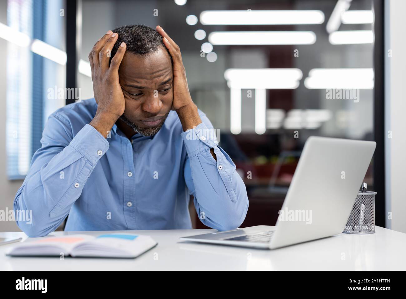 Employé de bureau stressé, les mains sur la tête, travaillant avec un ordinateur portable sur le bureau, éprouvant une pression élevée et de la fatigue. Concept de stress, de frustration, de pression sur les délais. Banque D'Images