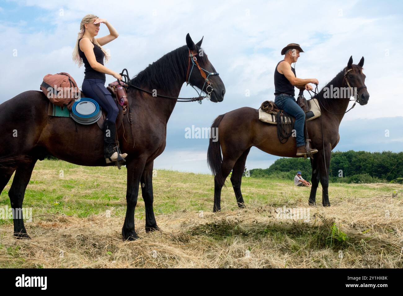 Deux cavaliers sur un terrain herbeux, une femme regardant au loin et un homme assis sur son cheval portant un chapeau Banque D'Images