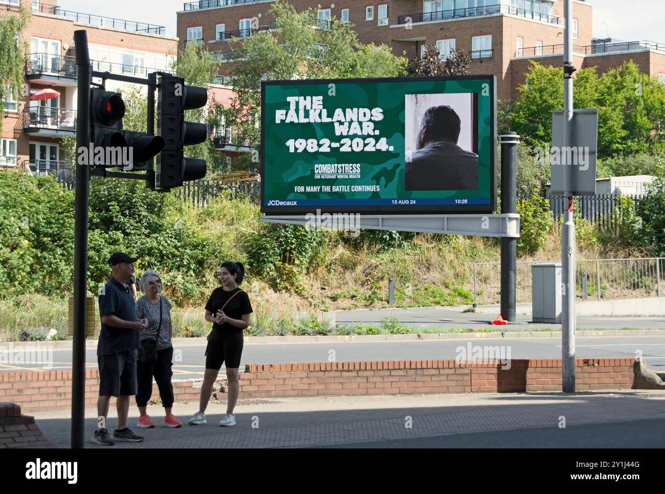 trois personnes attendent de traverser une route devant un panneau d'affichage numérique annonçant l'organisme de bienfaisance pour la santé mentale des anciens combattants, combat stress, à kingston, surrey Banque D'Images