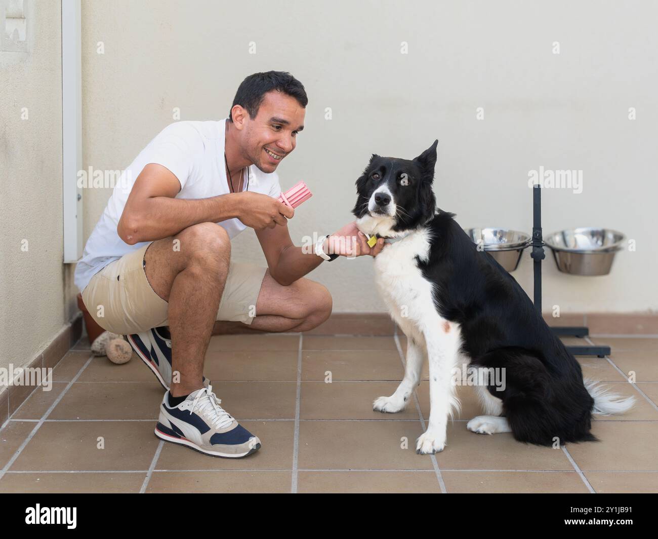 Un homme caresse un chien tout en tenant un bâton de glace rouge et blanc. Le chien est assis sur le sol et il apprécie l'attention Banque D'Images