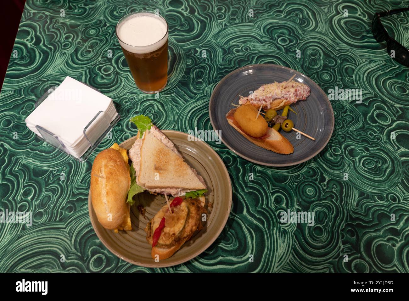 Pintxos espagnols au jambon, olives, poivron vert, omelette, crabe, morue et mayonnaise. Servi avec une bière blonde froide. Serviettes sur la table, avec une paire o Banque D'Images