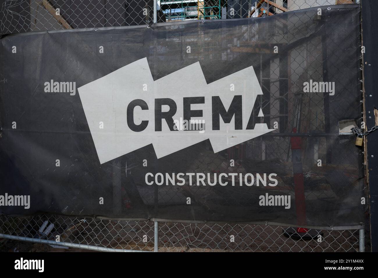 Bannière en maille noire et blanche Crema constructions, avec logo de la société, sur une porte de maillons de chaîne à l'extérieur d'un chantier de construction Banque D'Images