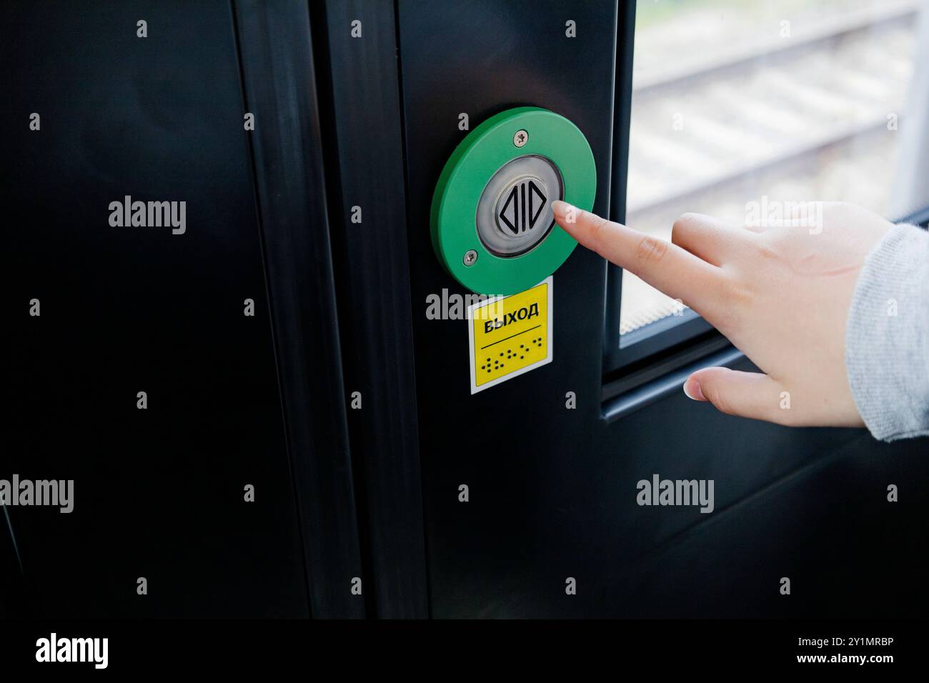 Une personne appuie sur un bouton vert vif situé sur une porte qui sert probablement de point d'entrée pour un bâtiment ou une pièce Banque D'Images