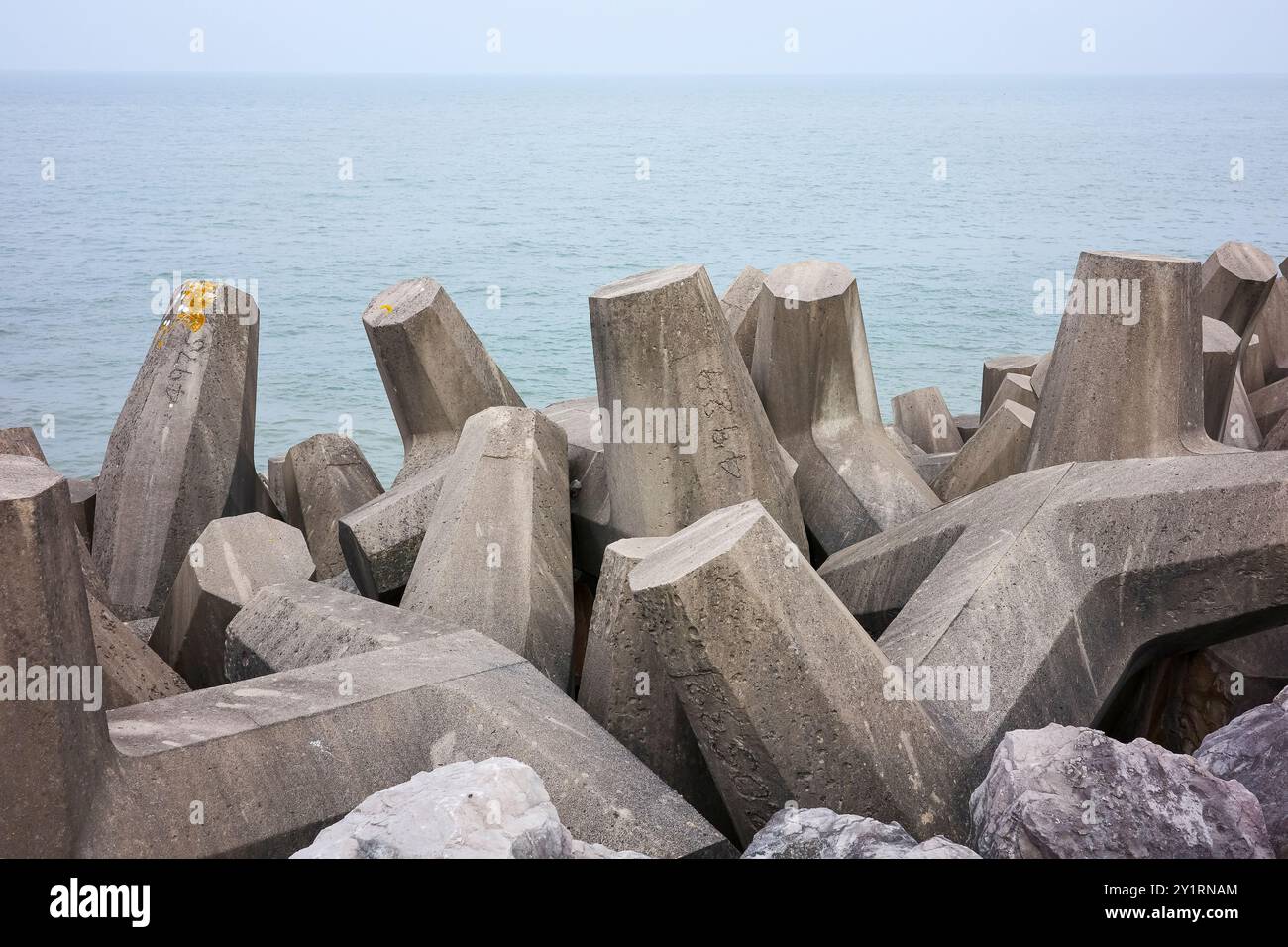 Défense maritime tétrapodes en béton sur une côte rocheuse contre une mer calme, renforçant la protection côtière. Banque D'Images