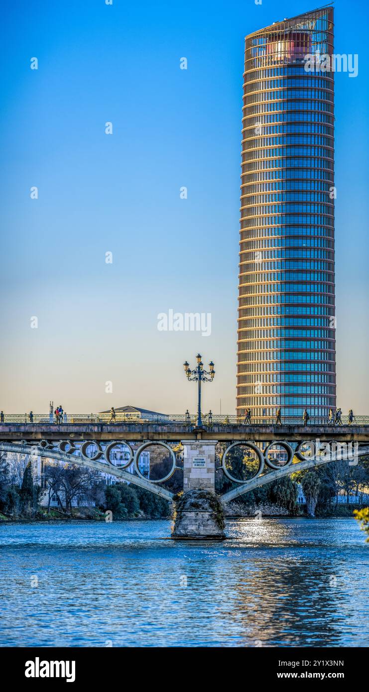 Une belle vue sur le pont Triana et Torre Sevilla reflétant sur la rivière sous un ciel clair du soir, mettant en valeur la beauté architecturale de Séville, Banque D'Images