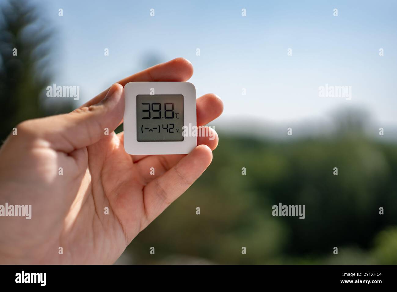 Un petit thermomètre est tenu dans une main humaine, affichant des températures estivales très élevées. La scène met en évidence l'impact du réchauffement climatique et tropical Banque D'Images