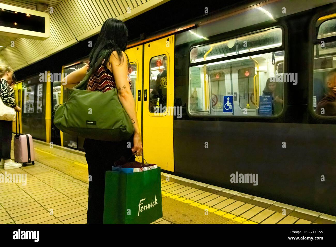 Une femme se tient debout sur la plate-forme du métro tenant des sacs à provisions à l'arrivée du train, avec des passagers à l'intérieur et le banlieue en arrière-plan. newcastle upon tyne Banque D'Images