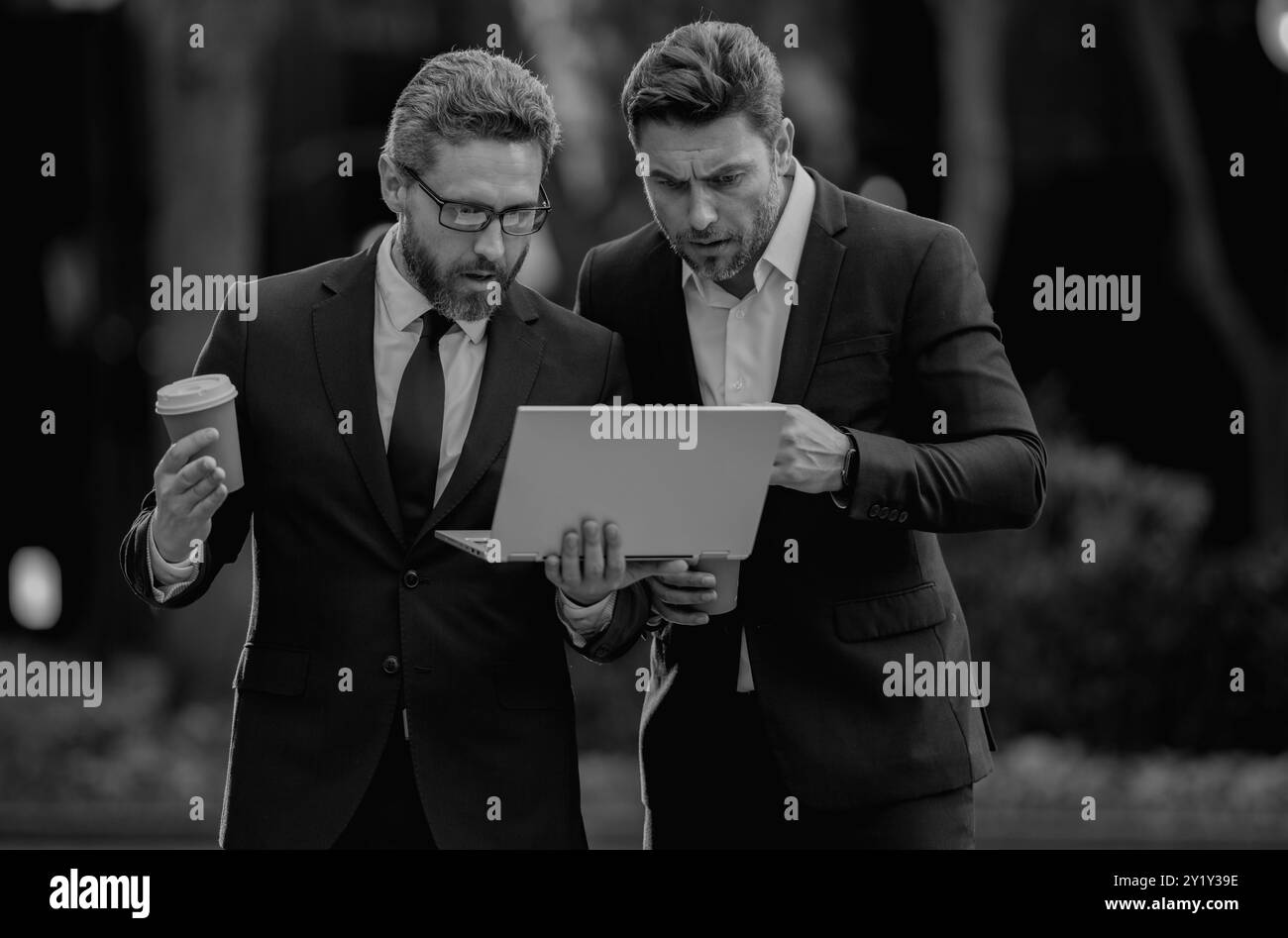 Deux beaux jeunes hommes d'affaires en costumes classiques à l'aide d'un ordinateur portable. Concept Freelance. Équipe d'hommes d'affaires utilisant un ordinateur portable à l'extérieur. Deux hommes parlant en ville urbaine Banque D'Images