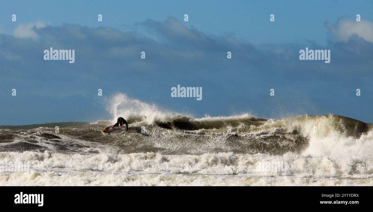 surfeur chevauchant vague dans l'océan sur planche de surf en mer avec bateau et ciel bleu en arrière-plan. Banque D'Images