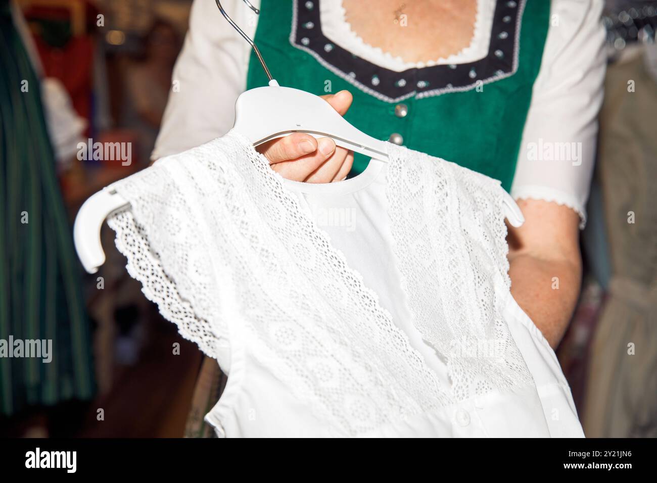 Gros plan d'une femme tenant une blouse en dentelle blanche sur un cintre avec une robe traditionnelle en arrière-plan, mode, concept de vêtements Banque D'Images