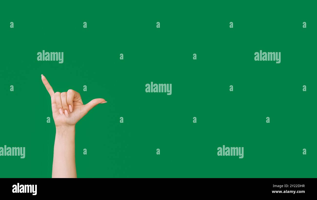 Signe Shaka. Geste d'appel. Accrochez-vous. Signe de sonnerie de téléphone. Main féminine montrant le signal de salutation isolé sur fond d'espace vide vert. Banque D'Images