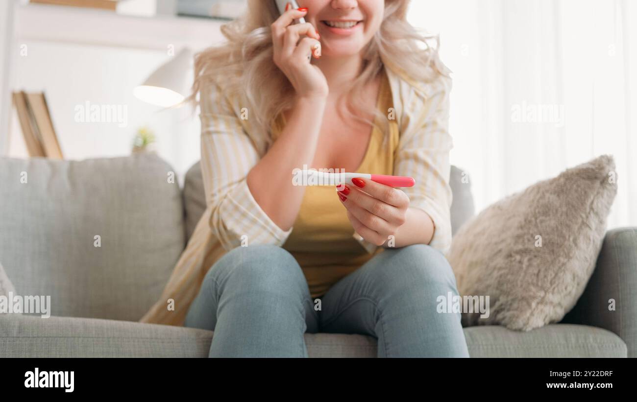 Bonne maternité. Femme joyeuse. Partage des actualités. Dame excitée parlant du test de grossesse positif par smartphone assis canapé lumière intérieur de la pièce. Banque D'Images