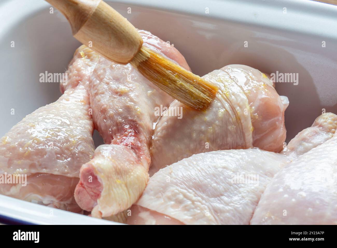 Glaçage du poulet cru avec un glaçage au citron et au miel avec un pinceau. Dans un plat en émail sur une planche de bois. Banque D'Images