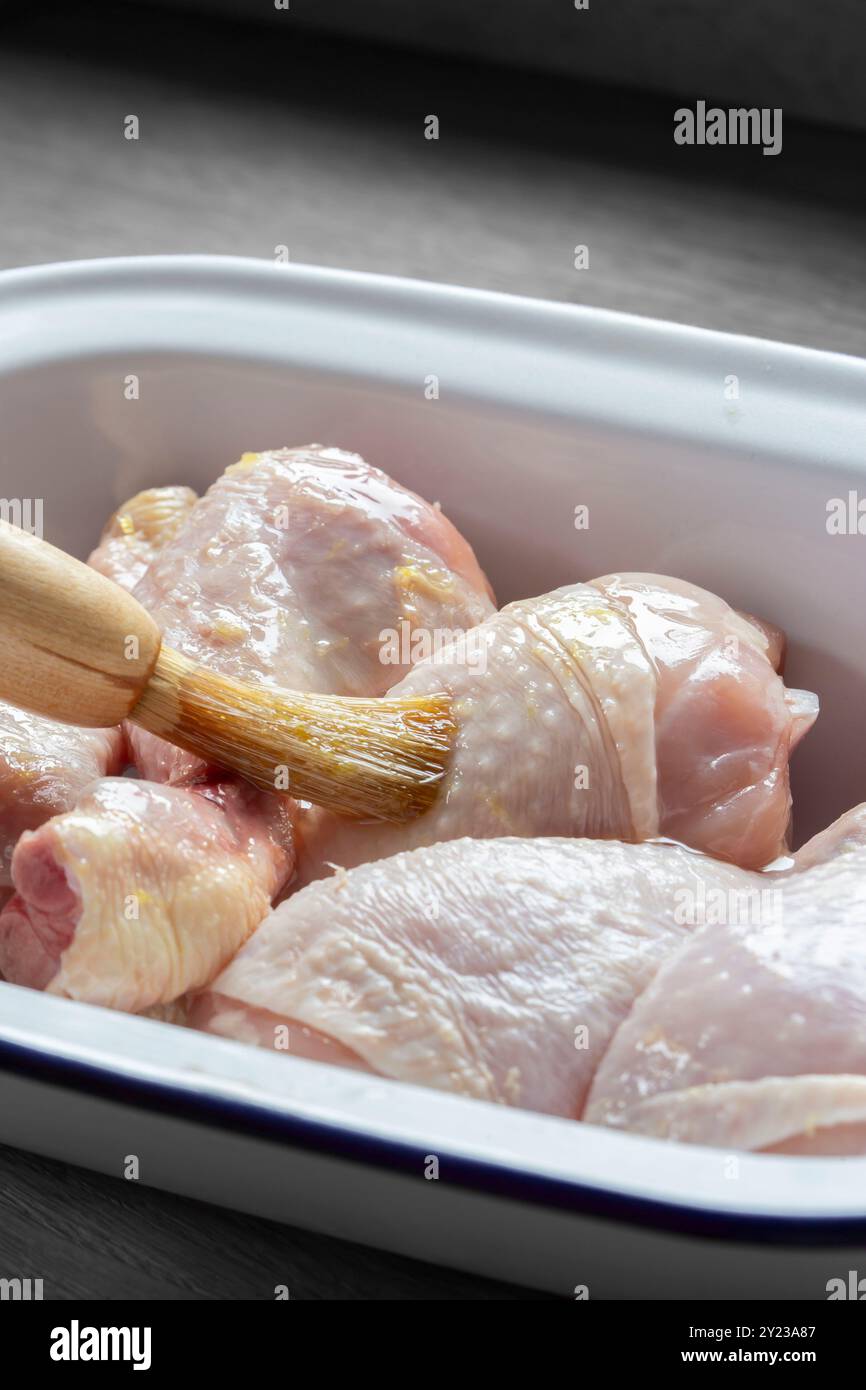 Glaçage du poulet cru avec un glaçage au citron et au miel avec un pinceau. Dans un plat en émail sur une planche de bois. Banque D'Images