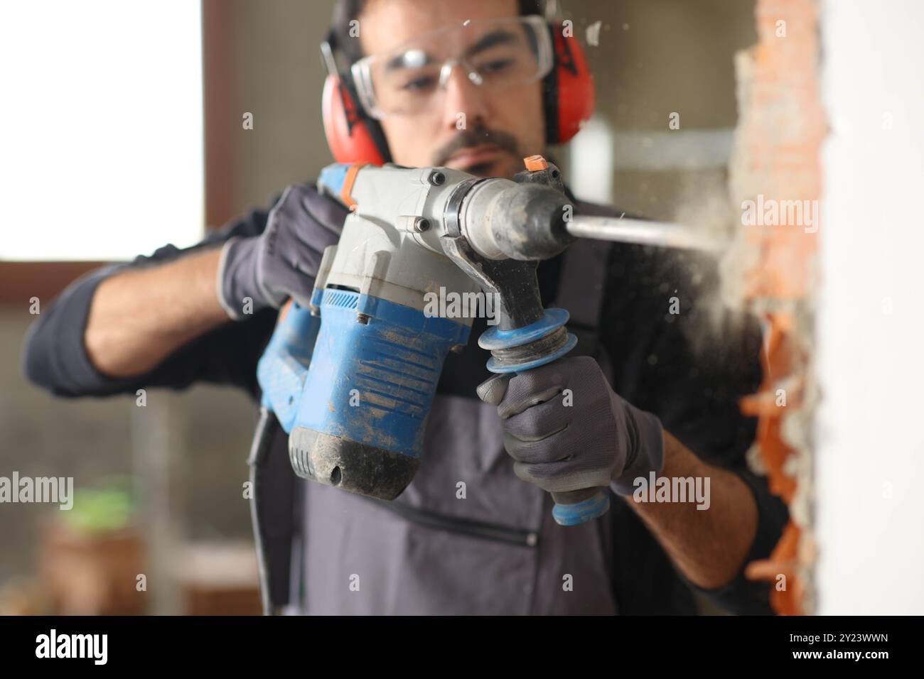 Travailleur de la construction travaillant le mur de démolition à l'aide d'un marteau rotatif dans une maison en rénovation Banque D'Images