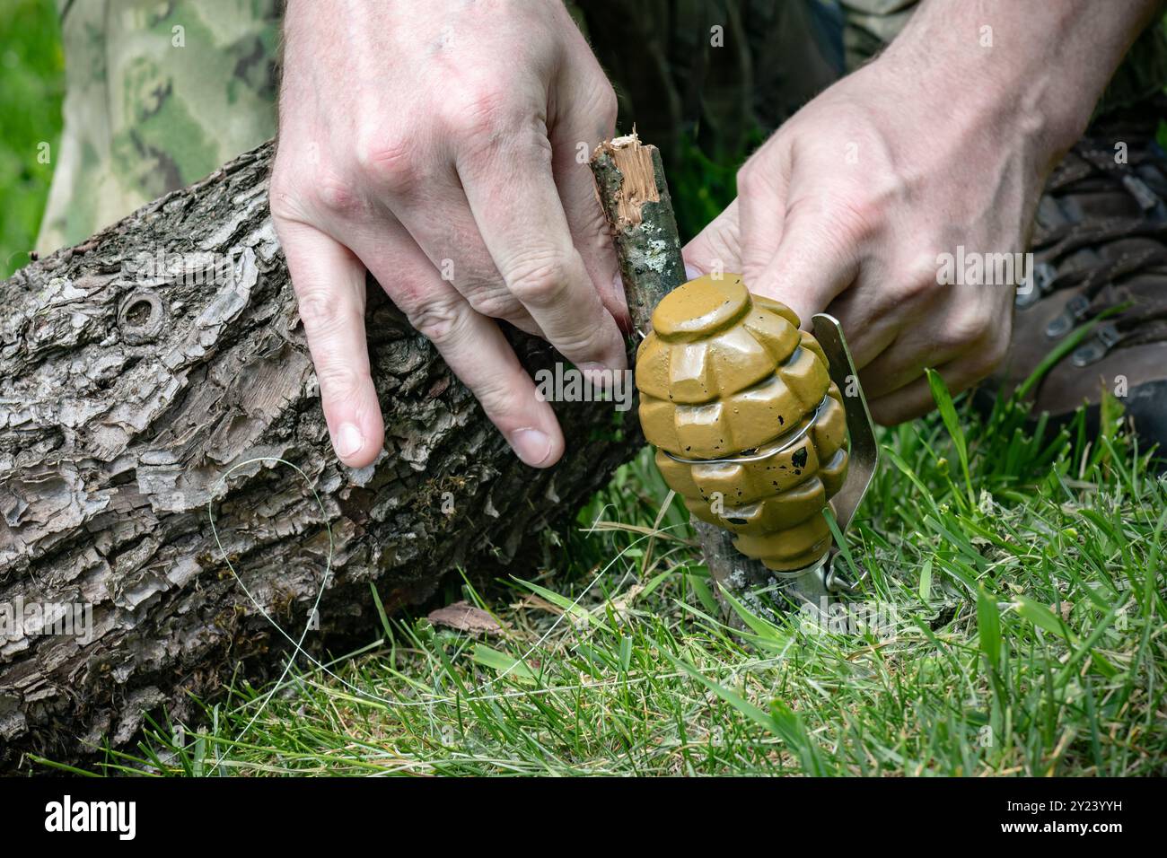 Un homme est en train d'intresser une mine terrestre Booby Trap faite par les mains de grenade à main avec tripwire sur le sol près des mains en bois de rondins en gros plan Banque D'Images