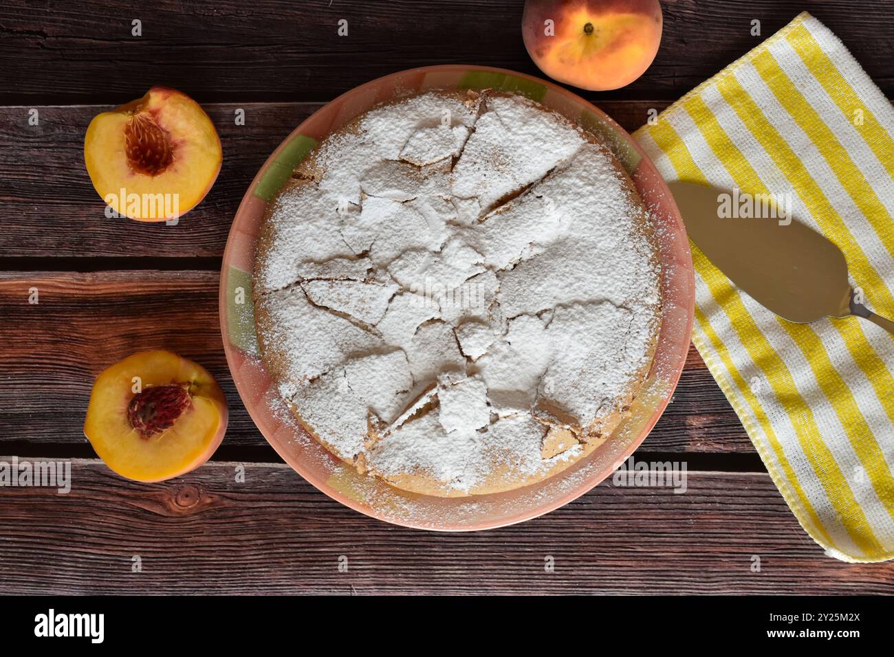 Tarte charlotte maison fraîchement cuite avec des pêches sur une table en bois. Gâteau saupoudré de sucre en poudre, pelle à gâteau en métal sur serviette rayée. Vue de dessus. Banque D'Images