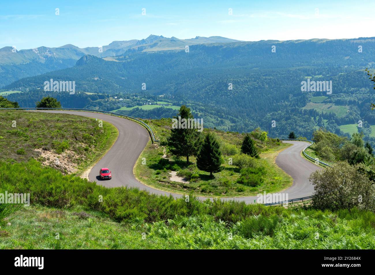 Route sinueuse dans le Parc naturel régional des volcans d'Auvergne avec le massif du Sancy en arrière-plan, Puy de Dôme, Auvergne, France Banque D'Images
