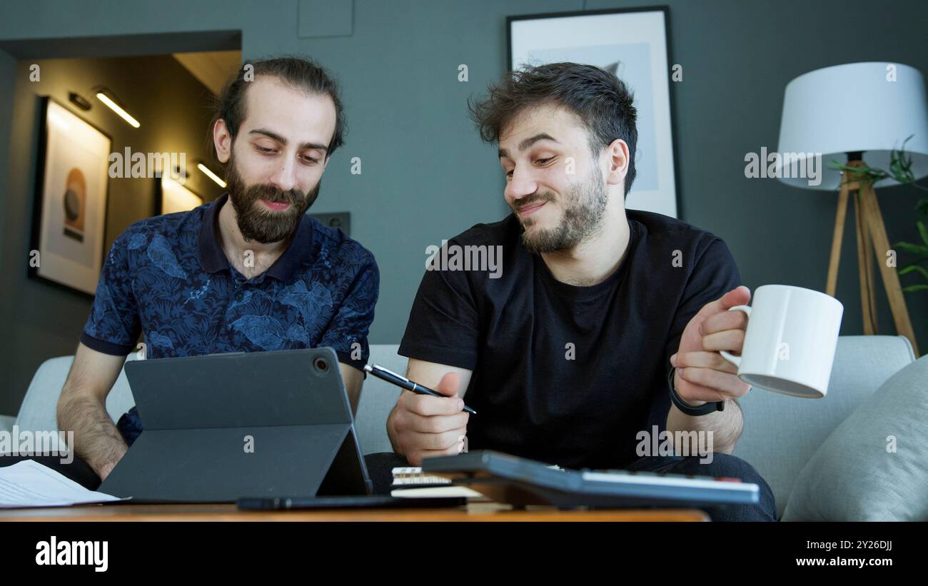 Deux hommes sont assis sur un canapé, collaborant à un projet. L'homme barbu avec une expression mécontente, critique le travail fait par son ami. Banque D'Images