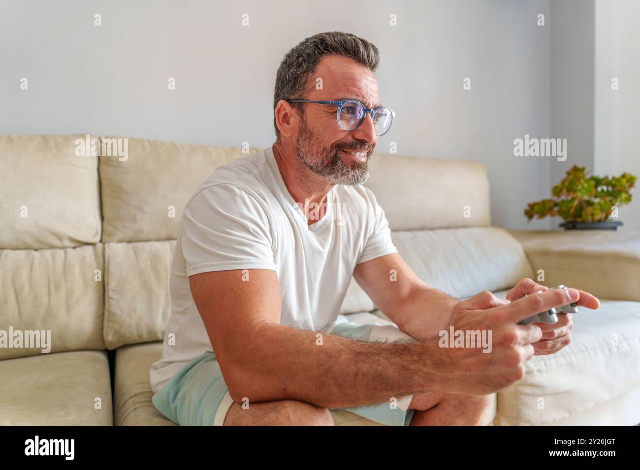 Homme d'âge moyen souriant tout en jouant à des jeux vidéo sur le canapé à la maison Banque D'Images