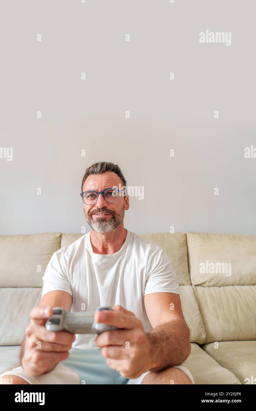 Vue avant de l'homme d'âge moyen souriant tout en jouant à des jeux vidéo sur le canapé à la maison Banque D'Images