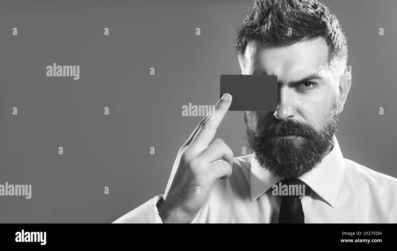 Bel homme d'affaires couvrant l'oeil avec carte de crédit ou de débit. Vente, finance, shopping et argent. Homme barbu sérieux avec carte bancaire ou financement de paiement Banque D'Images